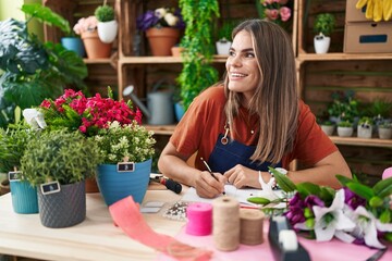 Young beautiful hispanic woman florist smiling confident writing on notebook at flower shop