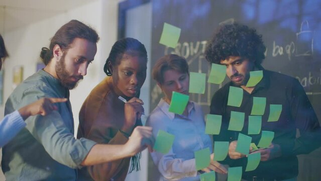 team of diverse creative multiethnic people studying strategy solutions using sticky notes on glass wall