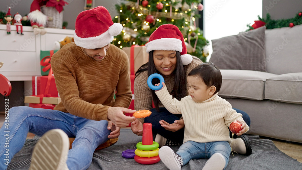 Poster couple and son sitting on floor by christmas tree playing with hoops toy at home