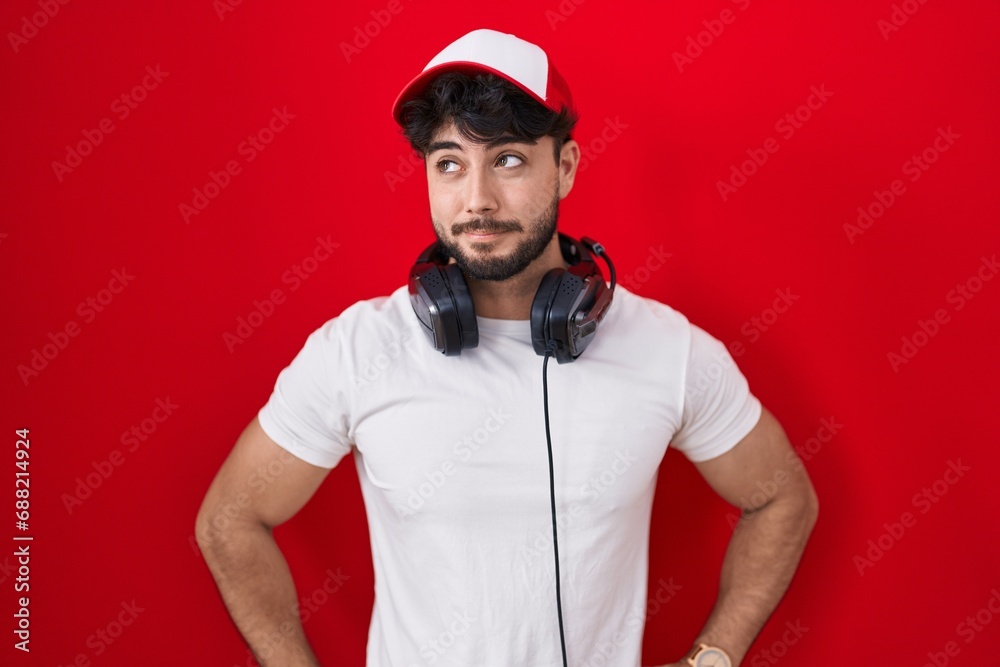 Sticker hispanic man with beard wearing gamer hat and headphones smiling looking to the side and staring awa