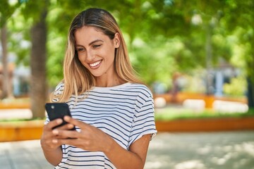 Young blonde woman smiling confident using smartphone at park