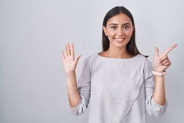 Young hispanic woman standing over white background showing and pointing up with fingers number seven while smiling confident and happy.