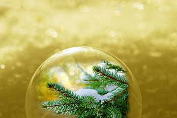 Weihnachtlicher goldener Hintergrund mit glitzernden Schneeflocken und Tannenzweigen in einer Kugel