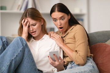 Depressed lady showing distressing phone message to shocked friend indoors
