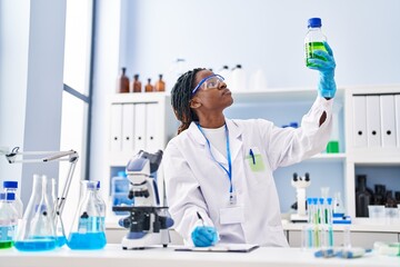 Fototapeta premium African american woman scientist holding bottle writing on document at laboratory