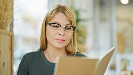 Young blonde woman smiling confident reading book at coffee shop
