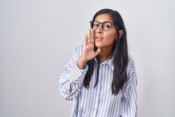 Young hispanic woman wearing glasses hand on mouth telling secret rumor, whispering malicious talk conversation