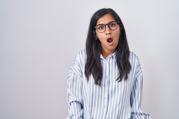 Young hispanic woman wearing glasses in shock face, looking skeptical and sarcastic, surprised with open mouth