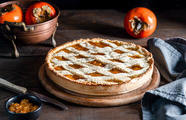 Italian homemade persimmon tart or crostata with ingredients on the wooden table, chiaroscuro