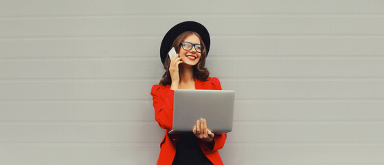 Businesswoman working with laptop calling on mobile phone wearing red blazer jacket, eyeglasses,...