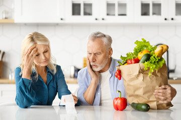 Concerned senior couple examining grocery bill after food shopping