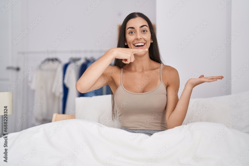 Sticker young brunette woman in the bed at home amazed and smiling to the camera while presenting with hand 