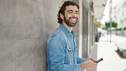 Obraz premium Young hispanic man using smartphone smiling at street