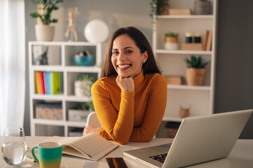 Cheerful businesswoman at desk with laptop at home office.