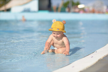 a little half a year old, a baby baby crawling on the water, smiling, outdoors, in a panama hat, in diapers, in the sun at the resort.