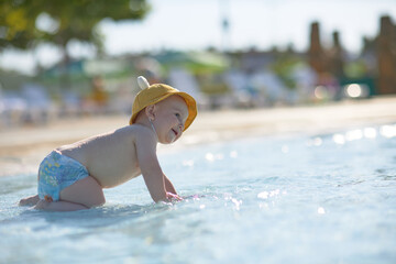 a little half a year old, a baby baby crawling on the water, smiling, outdoors, in a panama hat, in diapers, in the sun at the resort.
