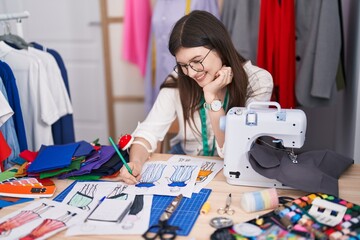 Young caucasian woman tailor smiling confident drawing clothing design at tailor shop