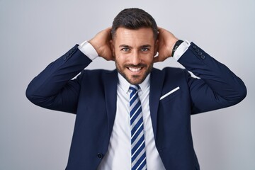 Handsome hispanic man wearing suit and tie relaxing and stretching, arms and hands behind head and neck smiling happy