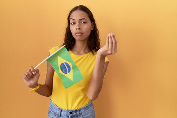 Young hispanic woman holding brazil flag doing italian gesture with hand and fingers confident expression
