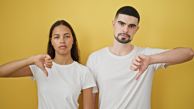Uncool vibes &acirc;&euro;&ldquo; beautiful couple together, seriously thumbs-down, against a strikingly yellow isolated wall