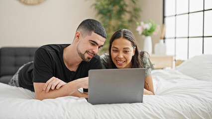 Adorable couple smiling and relaxing at home, lying in bed chatting and enjoying a lovely video call in their cosy, beautifully designed bedroom. - obrazy, fototapety, plakaty