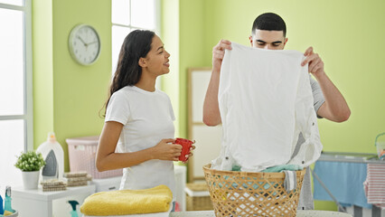 Beautiful, confident couple enjoy coffee while holding a basket of clothes in their home's laundry...