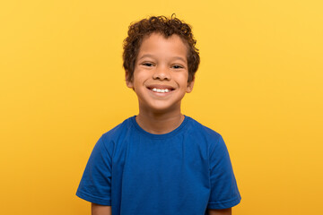 Happy black boy in blue shirt, yellow background