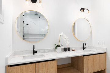 A bathroom with a floating white oak cabinet, white marble countertop, and black and gold lights...