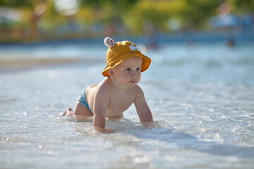 a little half a year old, a baby baby crawling on the water, smiling, outdoors, in a panama hat, in diapers, in the sun at the resort.