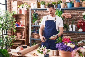 Young hispanic man florist cutting stem of flower at florist