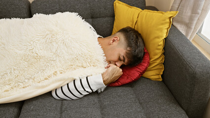 Exhausted, handsome young hispanic man finds comfort in a cozy nap, lying homebound on the sofa in...
