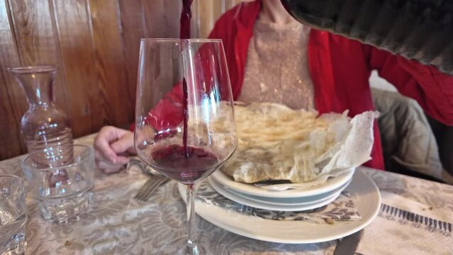 Pouring a glass of wine into a crystal glass, lady indulges in the symphony of flavors that is Borlengo, traditional dish from Italy's Emilia-Romagna, harmonizing meat and cheese in culinary delight.