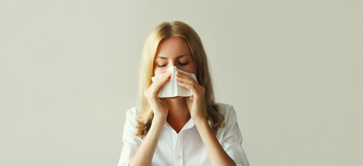 Sick exhausted caucasian young woman employee sneezing blow nose using tissue at home