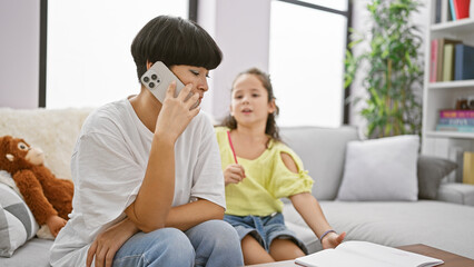 Mother and daughter bond over drawing on the sofa; mom balancing cellphone conversation and family time at home