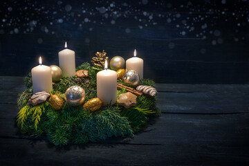 Green advent wreath with white candles, four are lit for fourth advent, Christmas decoration and cookies, dark blue wooden background with star bokeh, copy space
