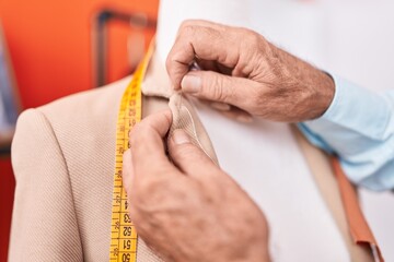 Middle age grey-haired man tailor sewing jacket on manikin at atelier