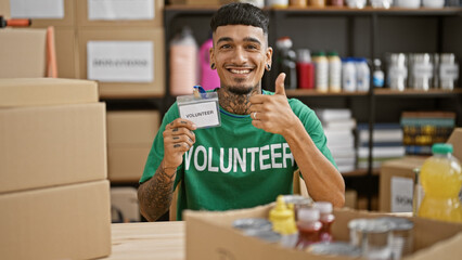 Confident young latin man, volunteering at charity center, wearing worker's uniform and a charming...