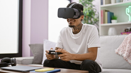 Confident young latin gamer happily using a joystick and vr glasses while playing intense video games in his comfortable living room - obrazy, fototapety, plakaty