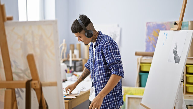 Portrait of a tattooed young latin man, an artist engrossed in his drawing, listening to inspiring audio on headphones in his art studio