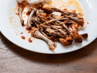 Pile of chicken wings bones on a white plate. Popular poultry product. Finished meal.
