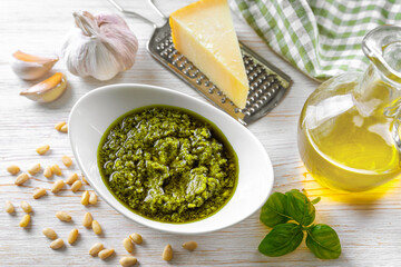 Homemade pesto sauce in small jar and ingredients for pasta on white wooden background with copy space. Traditional Italian cuisine, recipe, restaurant menu