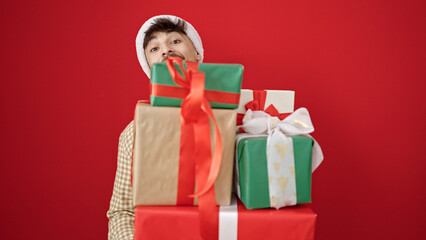 Young arab man wearing christmas hat holding lots of gifts over isolated red background