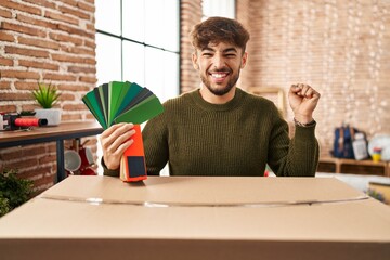 Arab man with beard moving to a new home choosing walls paint screaming proud, celebrating victory and success very excited with raised arm