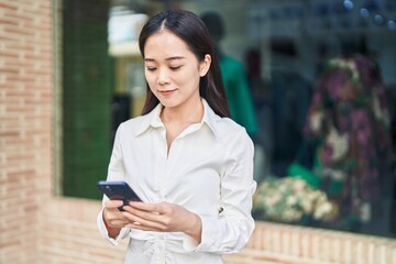 Young chinese woman smiling confident using smartphone at street