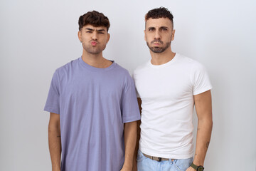 Homosexual gay couple standing over white background puffing cheeks with funny face. mouth inflated with air, crazy expression.