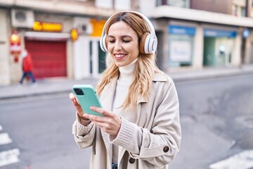 Young blonde woman listening to music at street