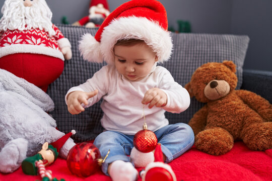 Adorable caucasian baby playing with christmas decoration ball sitting on sofa at home