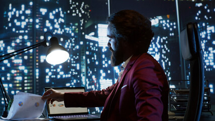Fototapeta na wymiar Executive director working at night in his skyscraper office building, examining global investment trends for new career opportunities. Influential businessman with billionaire vision checks reports.