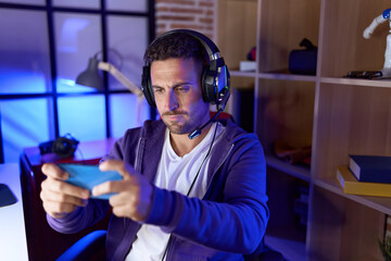 Young hispanic man streamer playing video game using smartphone at gaming room