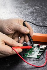 An electrician takes readings from a microcircuit using a multimeter. Measuring instruments. Copy space. Voltage measuring tool. Checking battery voltage. Male hands repairing a microcircuit.